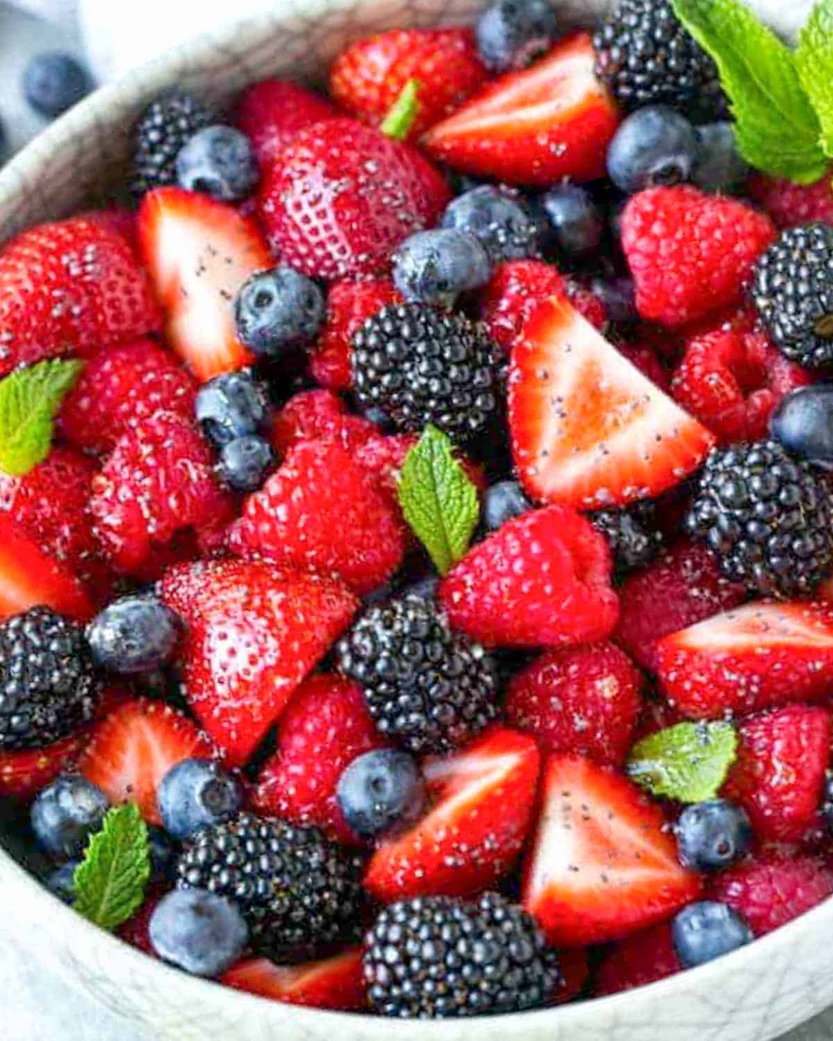 berries in a bowl with fresh mint and poppy seeds.