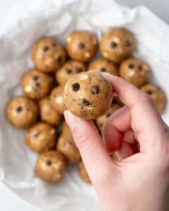 hand holding one peanut butter protein ball over a bowl.