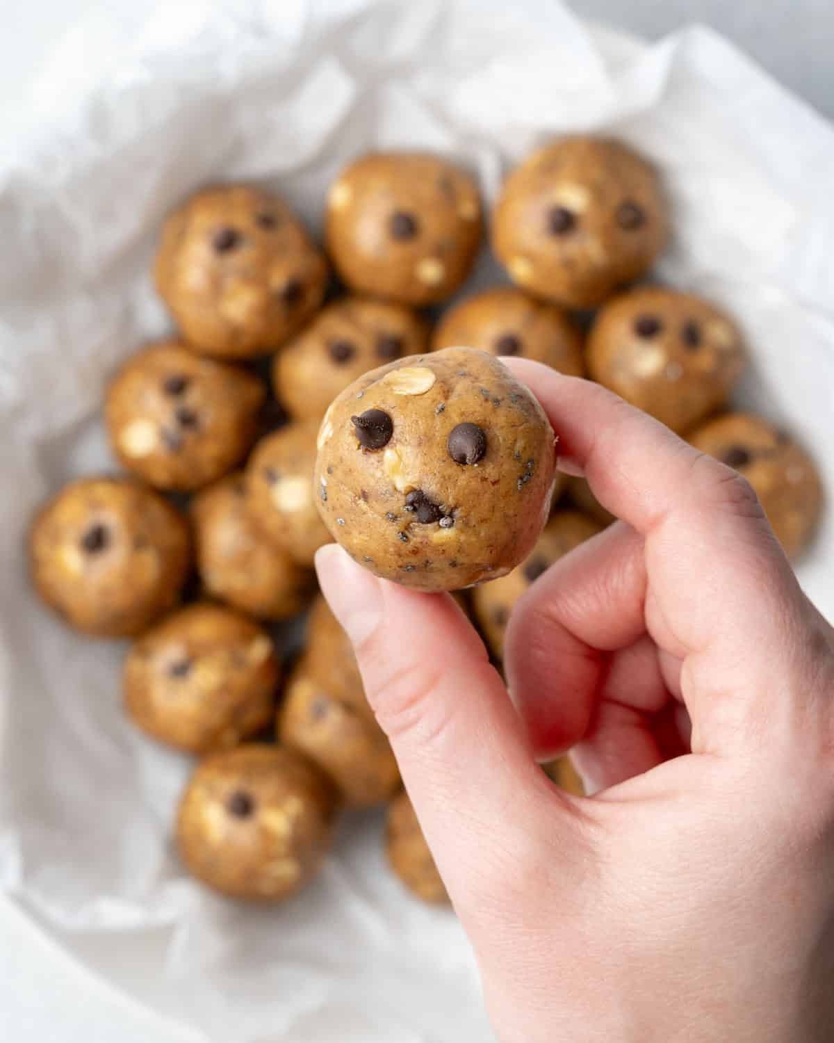 hand holding one peanut butter protein ball over a bowl.