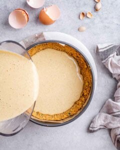 pouring pistachio cheesecake filling into graham cracker crust