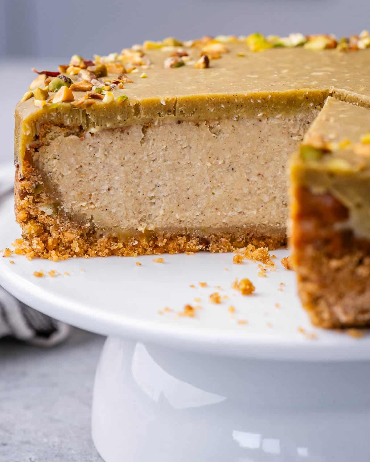 pistachio cheesecake on a white cake stand with a few slices taken