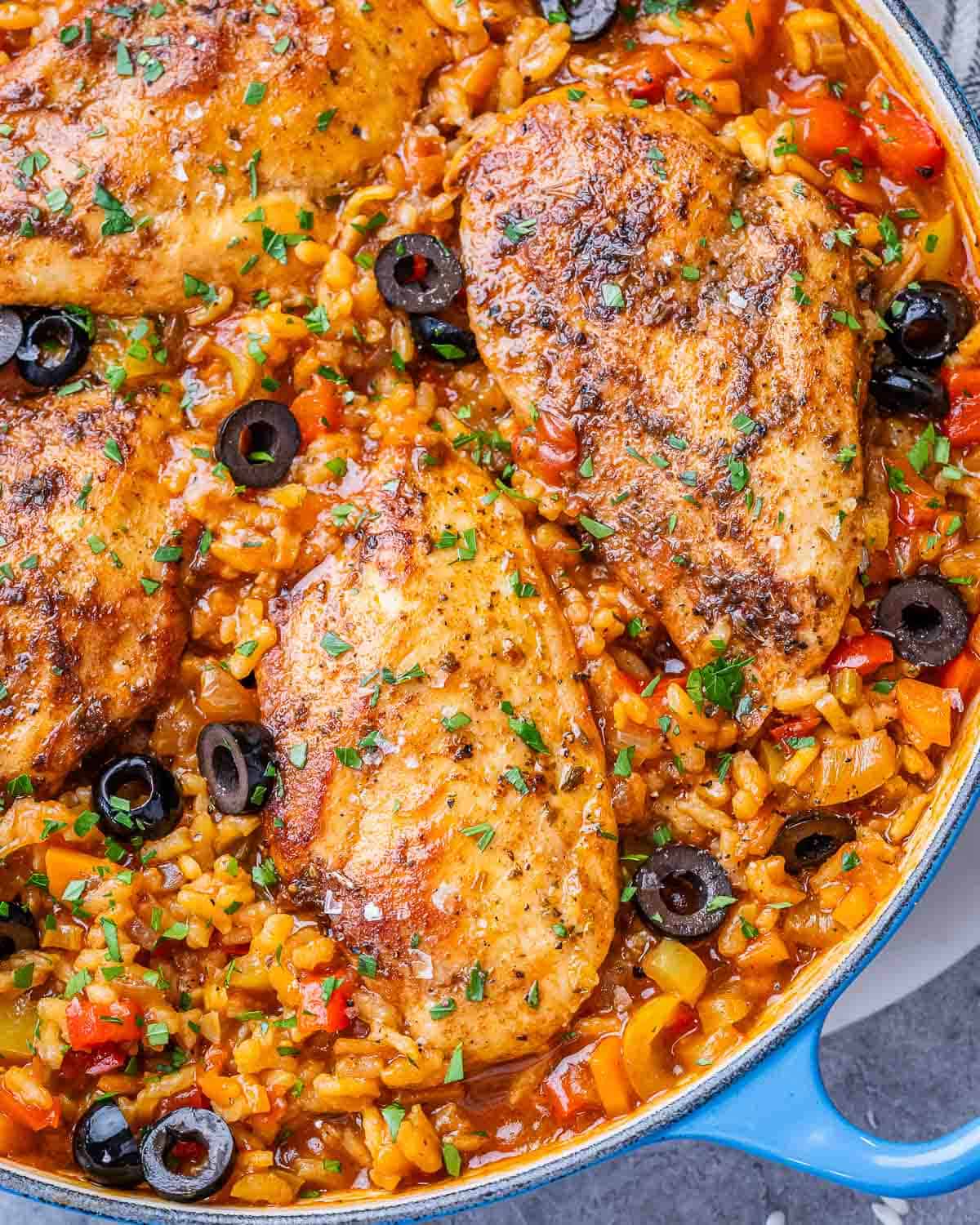 Skillet of Spanish chicken and rice with juicy chicken breasts, red and yellow peppers, and black olives.