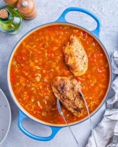Pan of simmering tomato sauce with chicken breasts being added in with tongs.