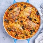 Overhead view of a skillet filled with Spanish chicken and rice, garnished with sliced black olives and fresh parsley.