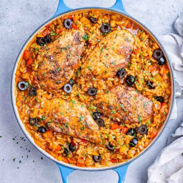 Overhead view of a skillet filled with Spanish chicken and rice, garnished with sliced black olives and fresh parsley.