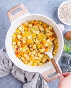 Stirring diced vegetables and seasonings together in a pot before adding broth and barley.