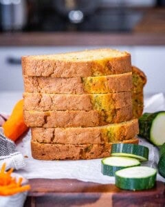 Stack of five thick slices of zucchini carrot bread with fresh produce in the background.