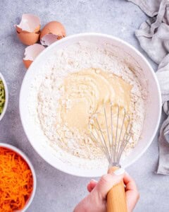 Final mixing stage of batter with flour just added, being whisked together with eggs, yogurt, and oil.