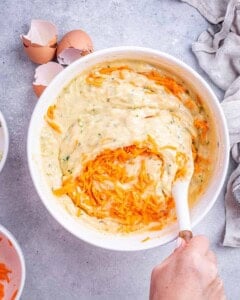 Bowl of batter with yogurt and oil just folded in, surrounded by eggs and carrots.