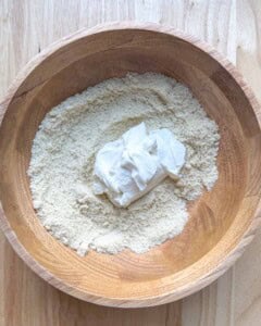 greek yogurt added over the almond flour mixture in a wooden bowl.