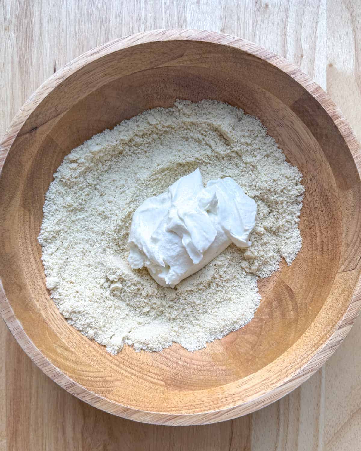 greek yogurt added over the almond flour mixture in a wooden bowl.