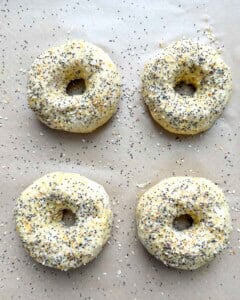 Uncooked bagels on a sheet pan, topped with everything bagel seasoning.
