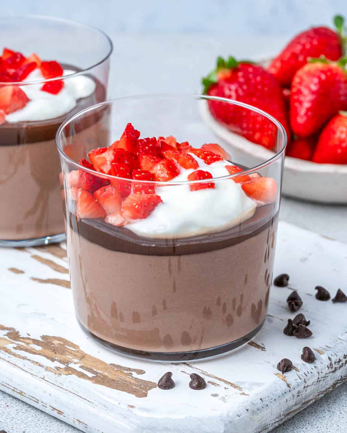 a cup with chocolate pudding topped with melted chocolate, whip cream, and chopped strawberries.
