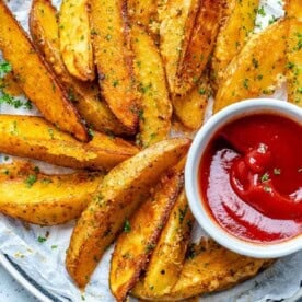 baked potato wedges on a plate served with a small bowl of ketchup.