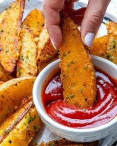 hand holding a potato wedge dipped in a bowl of ketchup.