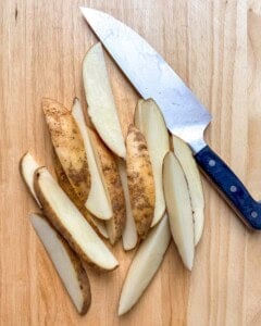 Potatoes cut into wedges on a cutting board.