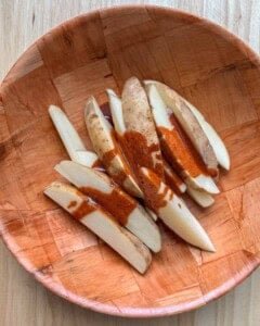 seasoning added over potato wedges in abowl.