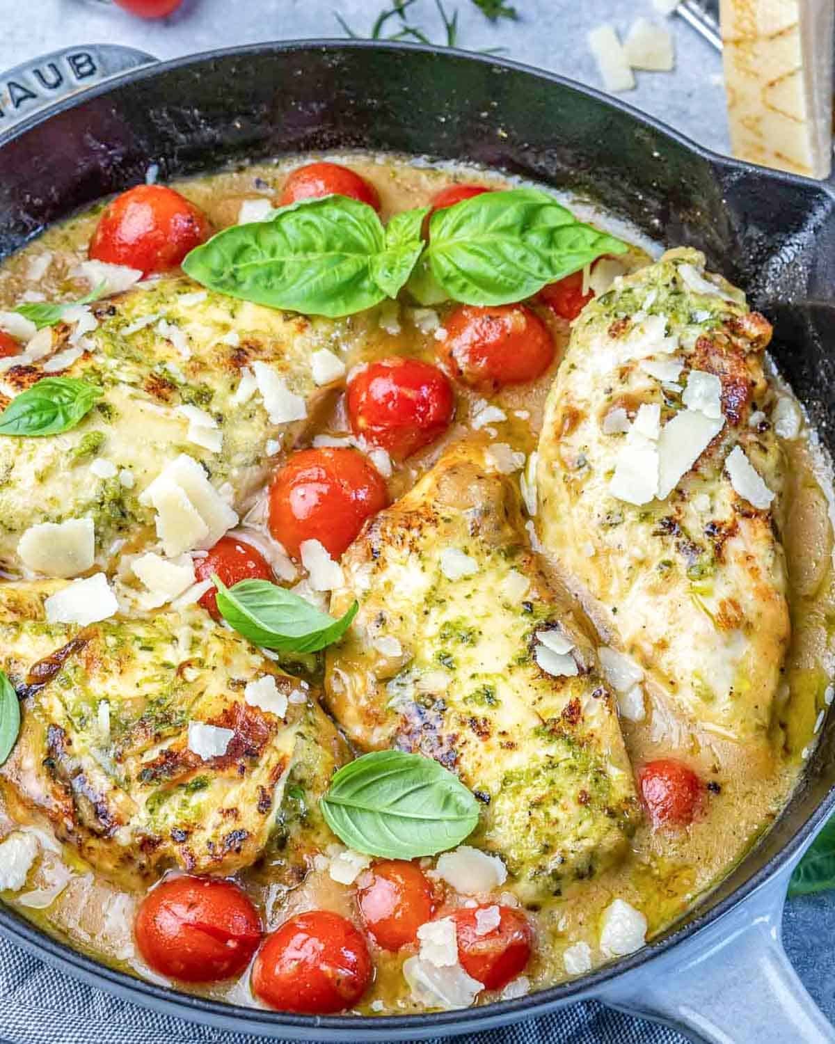 a skillet with baked pesto chicken with creamy sauce and tomatoes.