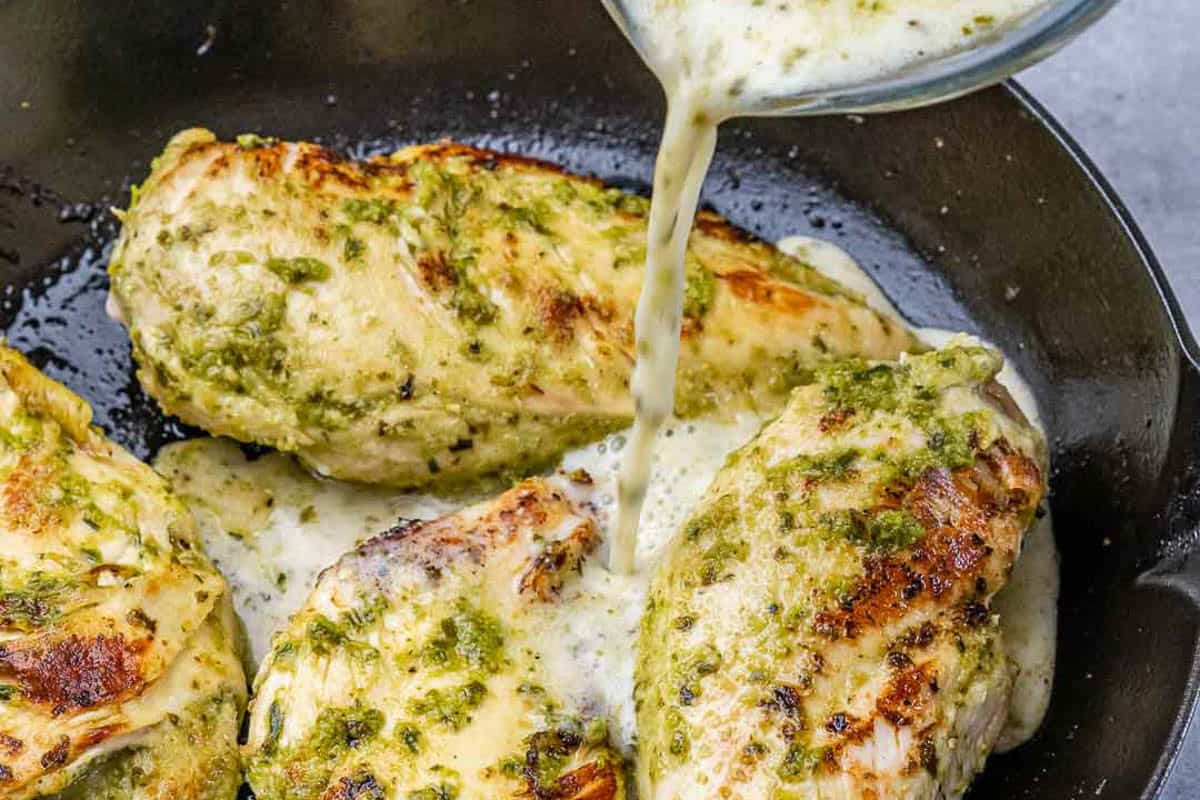 milk being poured over the cooked pesto chicken in the pan.