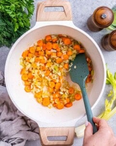 Chopped carrots, celery, onions, and garlic being sautéed in a pot with a spatula.