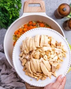 A plate of shredded rotisserie chicken being added into the pot for the soup.