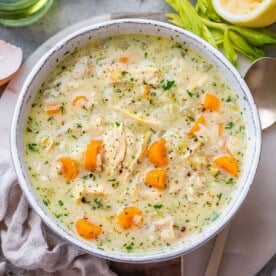 Top view of a pot of creamy Greek Avgolemono Soup filled with rice, carrots, and fresh herbs.