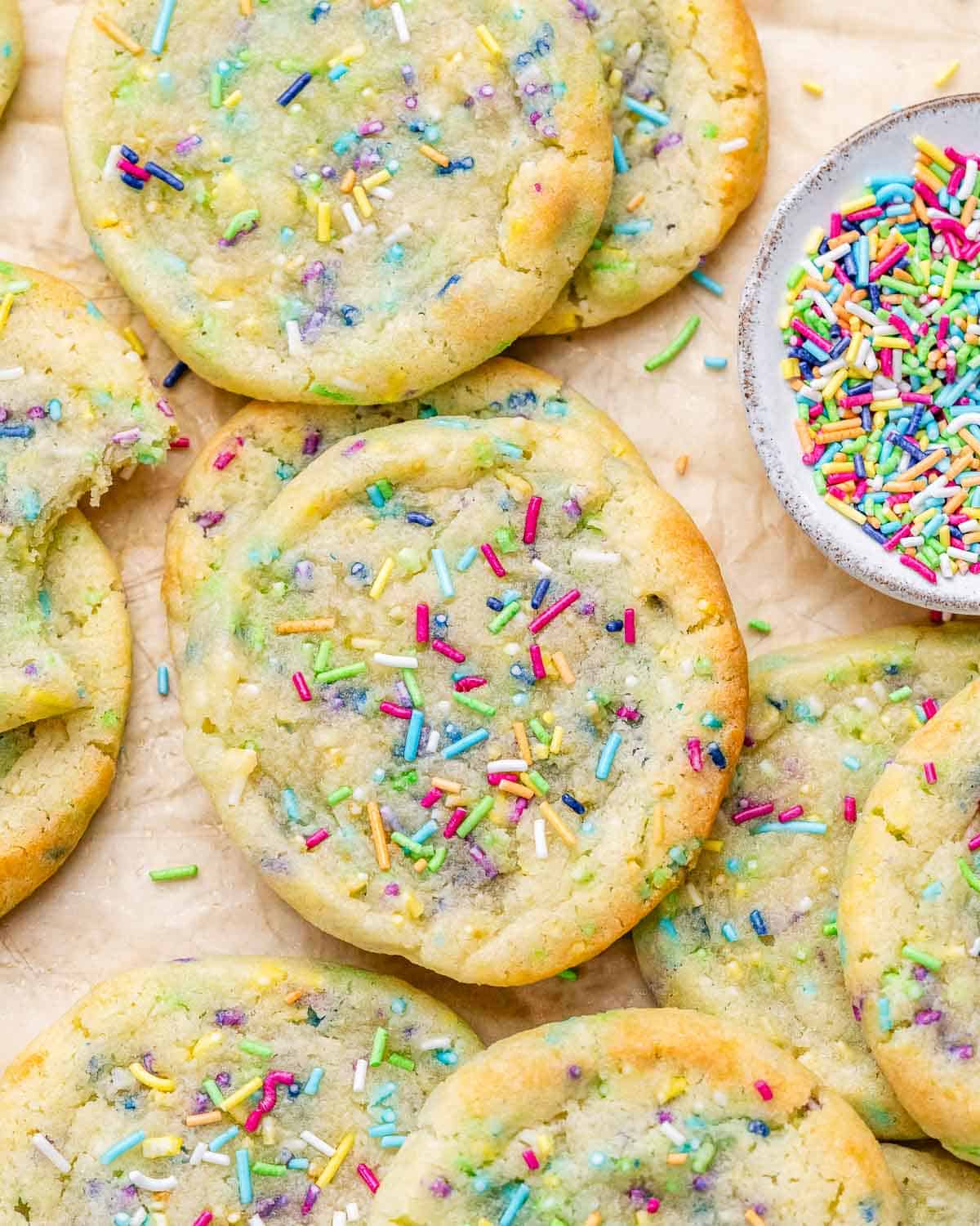 Cookies scattered on a sheet with a small bowl of sprinkles, showing the golden edges and soft texture.