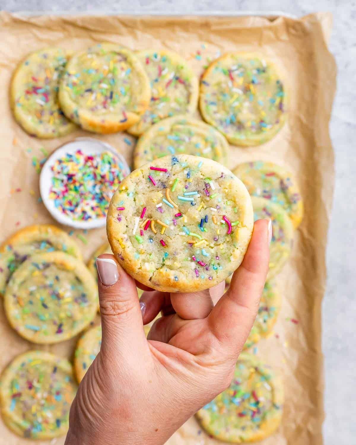 Hand holding a single chewy cookie to show the soft center and sprinkle topping.