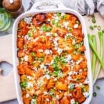 a casserole dish with chicken and potatoes with buffalo sauce, topped with sliced onions and blue cheese.