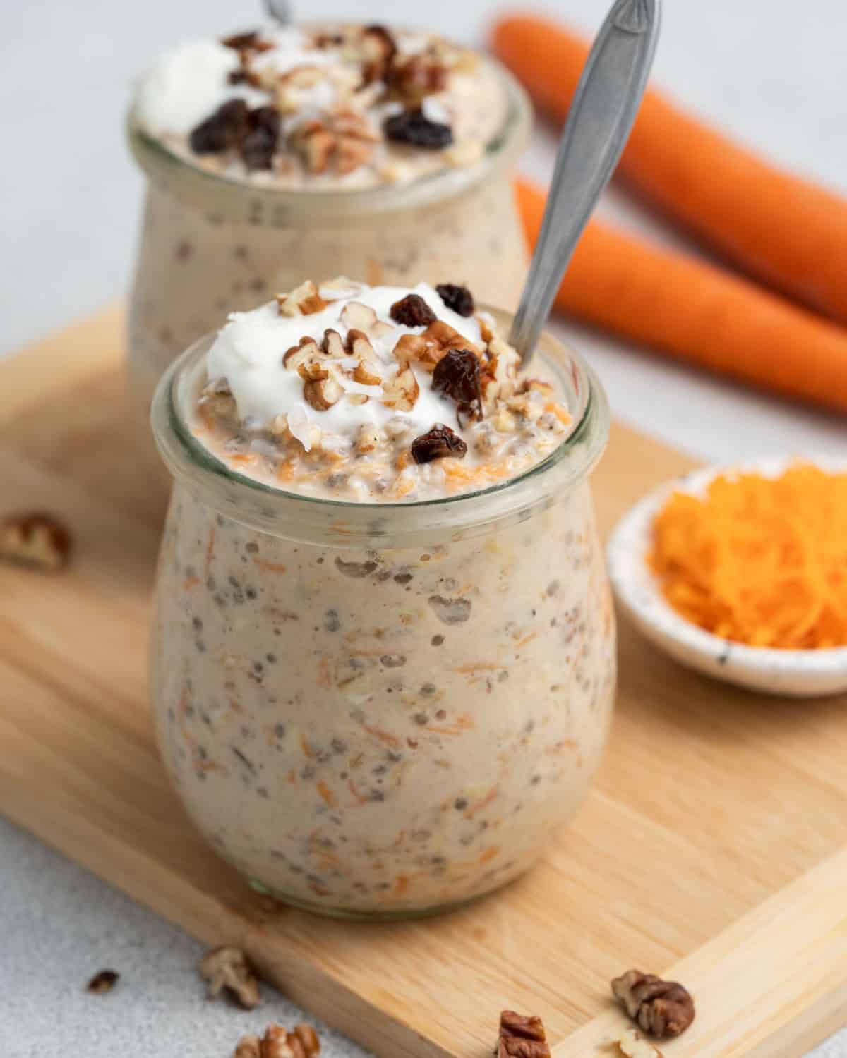 A jar of carrot cake overnight oats with a spoon on a wooden board.