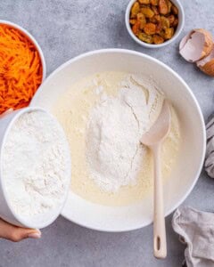 Flour being added into the wet ingredients in a mixing bowl with a wooden spoon.