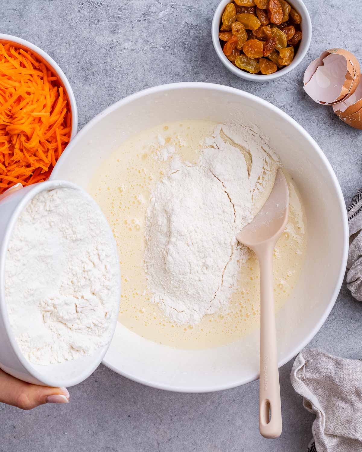 Flour being added into the wet ingredients in a mixing bowl with a wooden spoon.