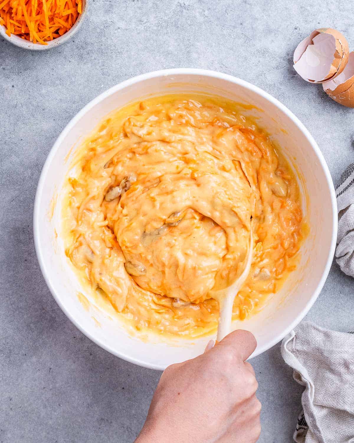 Mixing bowl with grated carrots and golden being stirred together with a wooden spoon.