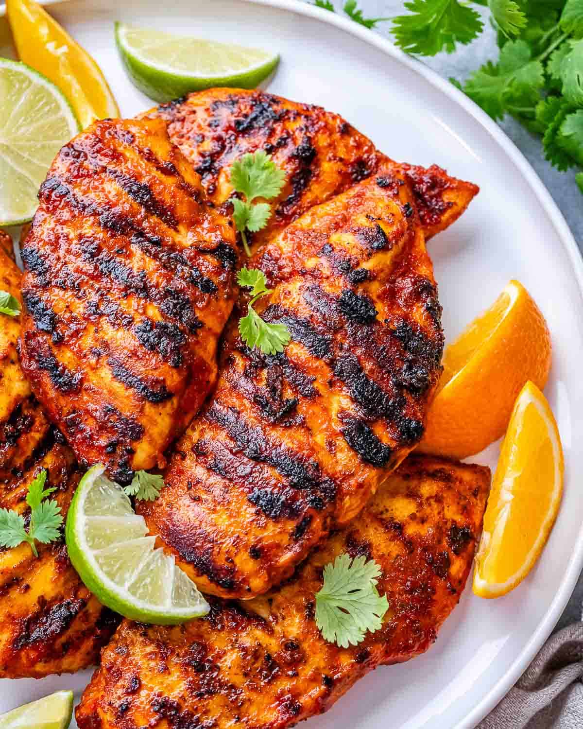 Grilled pollo asada chicken on a plate, garnished with lime wedges and fresh cilantro.