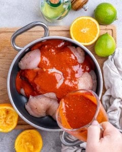 Fresh citrus marinade being poured over raw chicken breasts in a mixing bowl.
