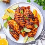 grilled chicken with asada sauce on a plate with lime and lemon wedges.