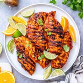 grilled chicken with asada sauce on a plate with lime and lemon wedges.
