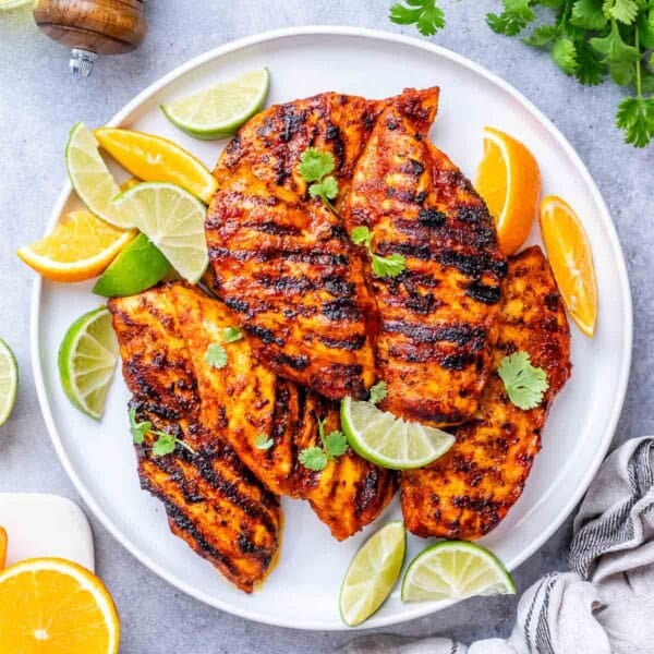 grilled chicken with asada sauce on a plate with lime and lemon wedges.