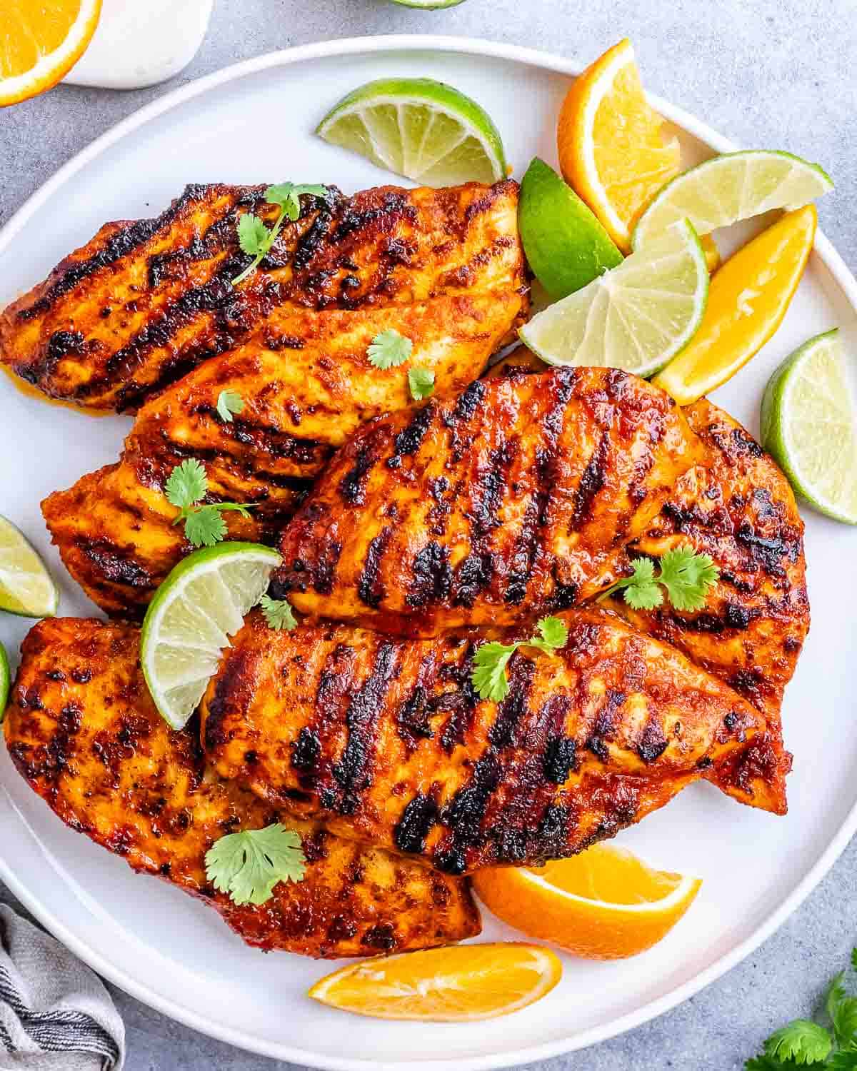 Close-up of charred, juicy chicken breasts cooked on the grill with orange and lime slices on the side.