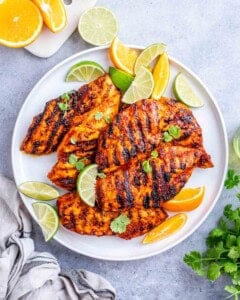 Plate of grilled pollo asada chicken served with lime wedges and cilantro for garnish.