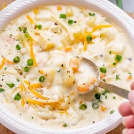 A spoon lifting a bite of cheesy potato soup garnished with green onions and cheddar.