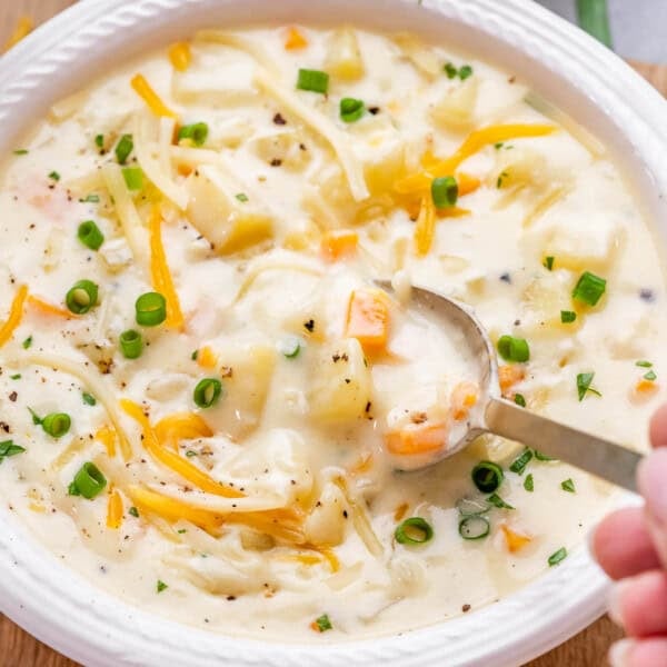 A spoon lifting a bite of cheesy potato soup garnished with green onions and cheddar.