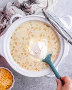 A scoop of cream cheese being added to the slow cooker with the cooked soup base.