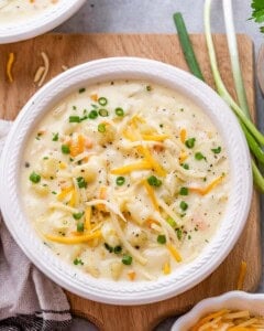 A bowl of potato soup topped with shredded cheddar cheese and sliced green onions.