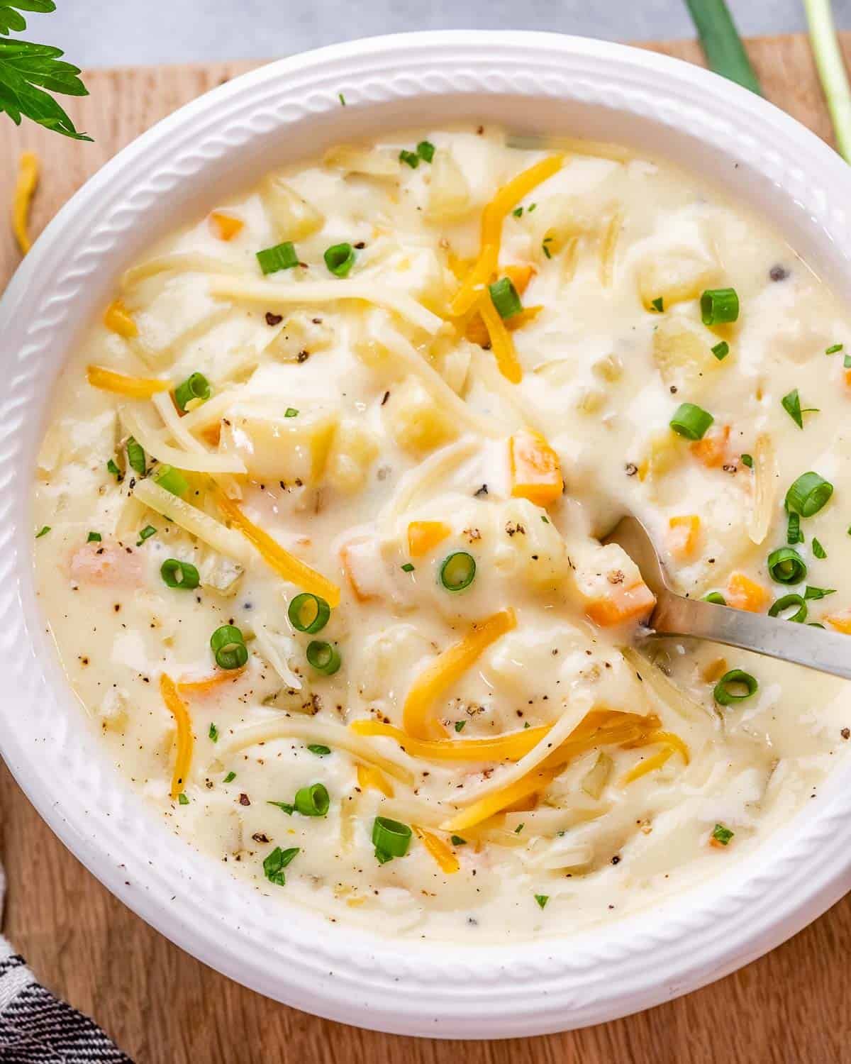 Close up top view of potato soup with melted cheese and chives sprinkled over the top, in a white bowl.
