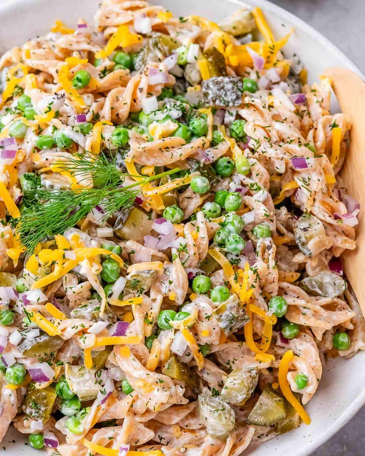Overhead view of dill pickle pasta salad, highlighting texture and color from red onion, cheese, and peas.