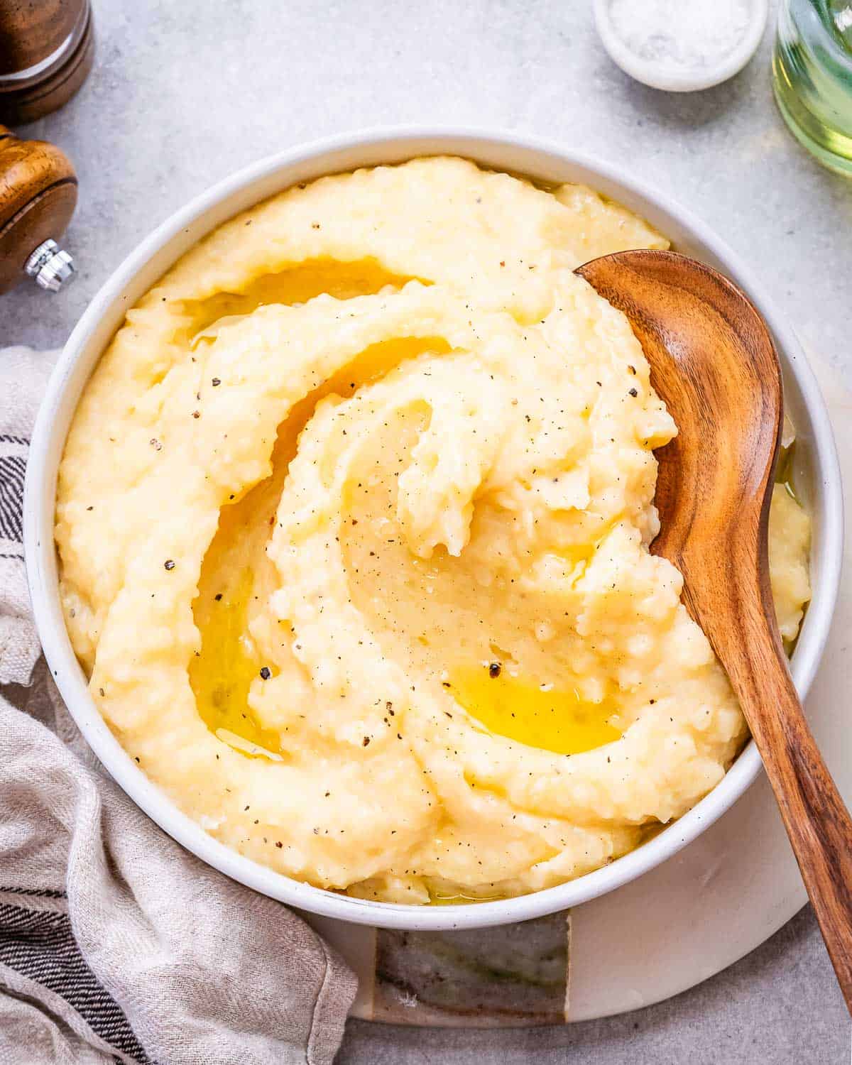 Mashed potatoes topped with melted butter, served in a white dish with a wooden spoon beside it.