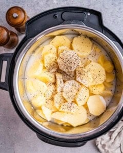 Pressure cooker pot with sliced potatoes seasoned generously with salt and black pepper.