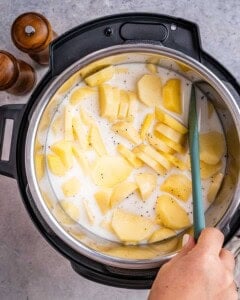 Instant Pot filled with sliced golden potatoes being stirred with a spatula before cooking.