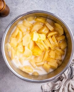 Instant Pot filled with cooked sliced Yukon gold potatoes with less milk mixture, and butter melting on top, ready for mashing.